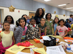 Children and staff smile in front of an art project